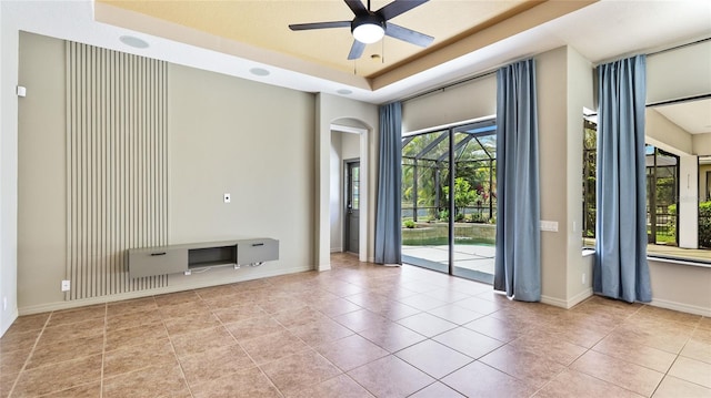 unfurnished living room with baseboards, a ceiling fan, a raised ceiling, arched walkways, and tile patterned flooring