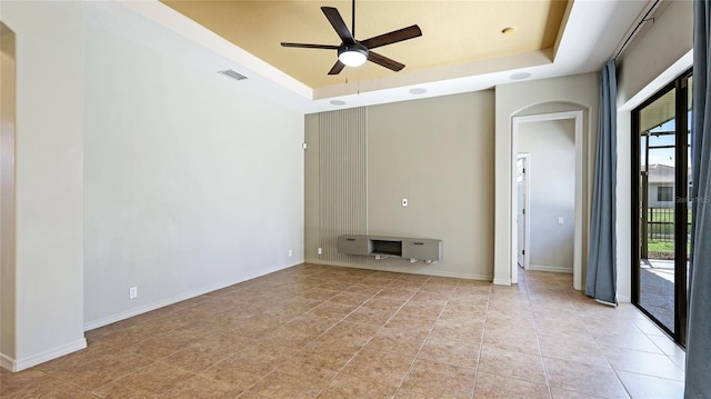 empty room with baseboards, a raised ceiling, arched walkways, visible vents, and a ceiling fan