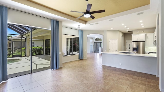 interior space featuring a tray ceiling, recessed lighting, light tile patterned floors, arched walkways, and a ceiling fan