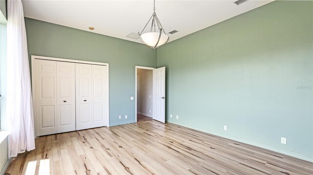 unfurnished bedroom with baseboards, a closet, light wood finished floors, and visible vents