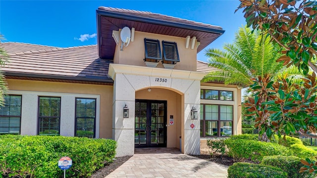 entrance to property with stucco siding, a tiled roof, and french doors