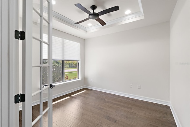 spare room featuring dark wood-type flooring, a tray ceiling, baseboards, and ornamental molding