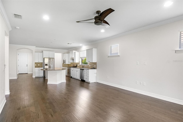 unfurnished living room with dark wood-type flooring, a ceiling fan, arched walkways, and crown molding