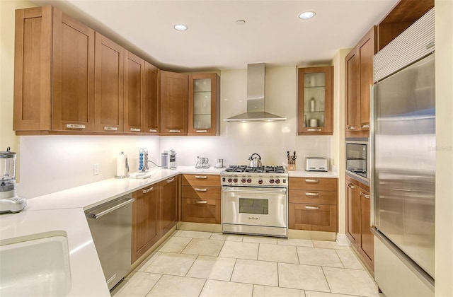 kitchen with wall chimney range hood, brown cabinets, built in appliances, and light countertops