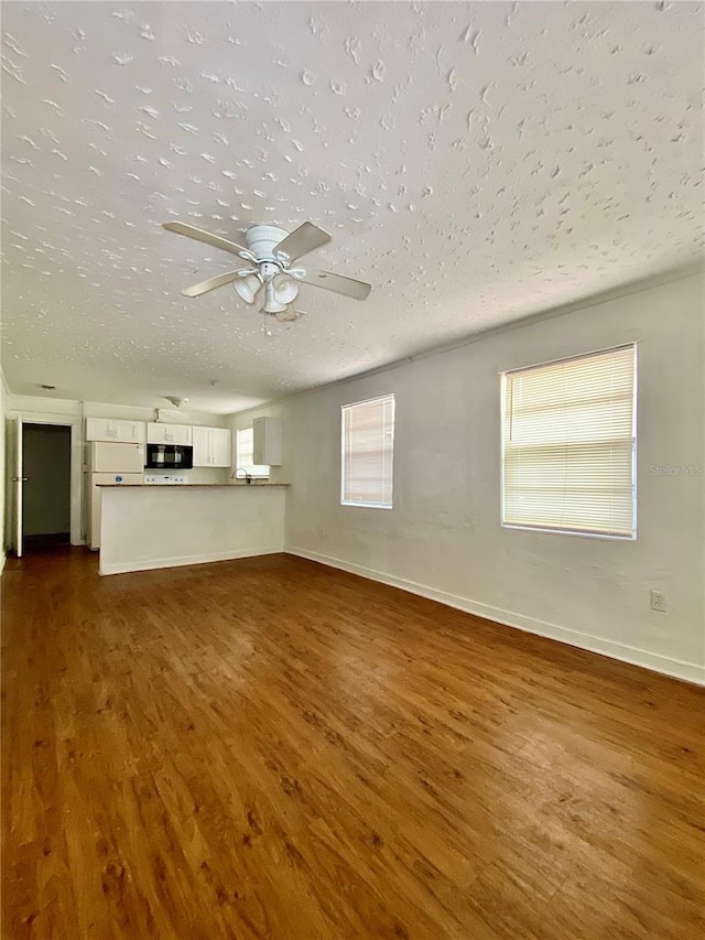 unfurnished living room with baseboards, dark wood-style flooring, a textured ceiling, and a ceiling fan