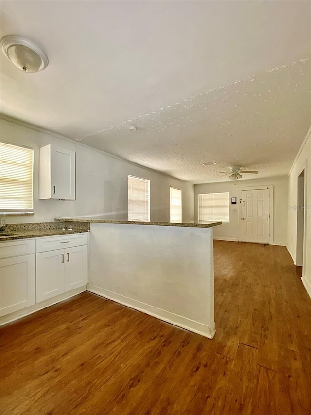 kitchen with a sink, a ceiling fan, a peninsula, white cabinets, and dark wood-type flooring