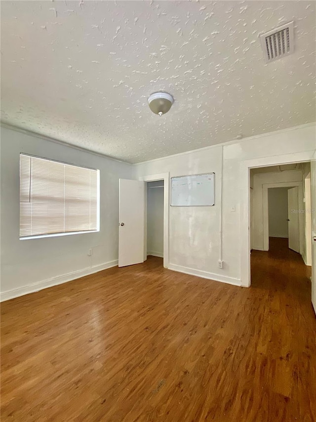 unfurnished bedroom with wood finished floors, a textured ceiling, baseboards, and visible vents