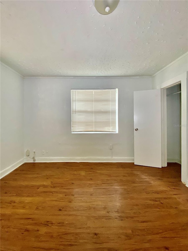 empty room featuring baseboards, a textured ceiling, wood finished floors, and crown molding