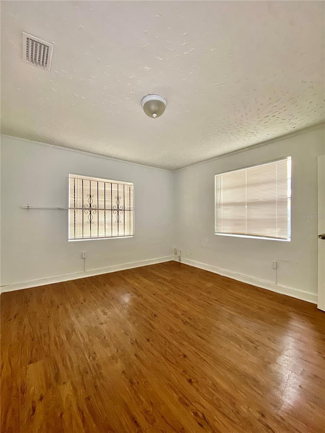spare room with baseboards, visible vents, wood finished floors, and a textured ceiling