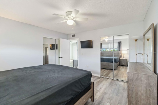 bedroom featuring baseboards, a textured ceiling, light wood-style floors, visible vents, and a ceiling fan