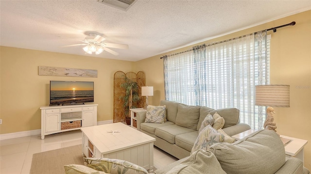 living area with light tile patterned flooring, a ceiling fan, visible vents, baseboards, and a textured ceiling