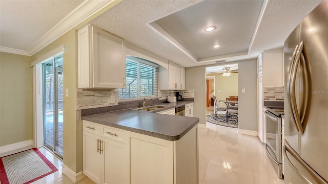kitchen with tasteful backsplash, stainless steel appliances, white cabinets, dark countertops, and a sink