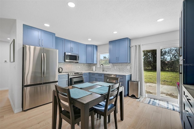 kitchen with backsplash, blue cabinetry, appliances with stainless steel finishes, and light wood finished floors