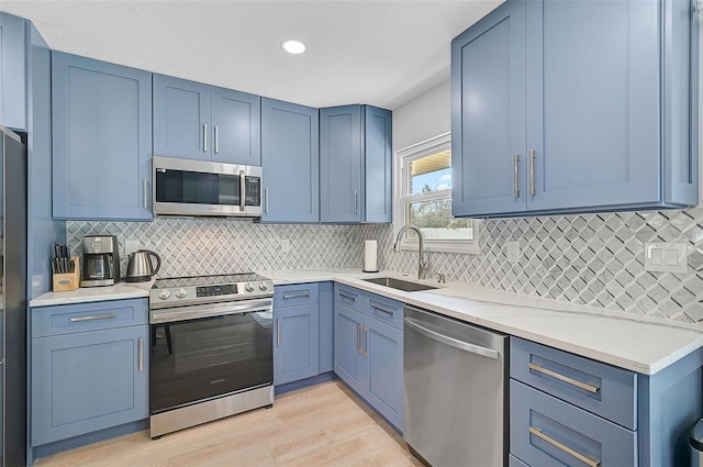 kitchen with a sink, appliances with stainless steel finishes, backsplash, and blue cabinetry