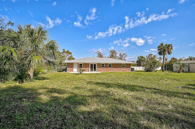 back of property with fence, a yard, metal roof, and brick siding