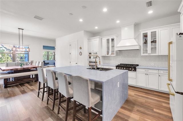 4308 Fly Rod Ter, Parrish, FL 34219 - kitchen with black cooktop, a sink, an island with sink, freestanding refrigerator, and custom range hood