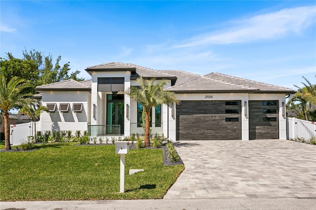 prairie-style home featuring stucco siding, fence, an attached garage, decorative driveway, and a front lawn