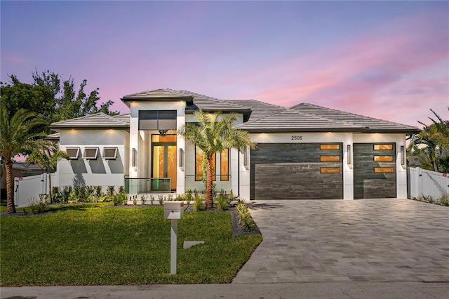 prairie-style home featuring driveway, stucco siding, an attached garage, fence, and a yard