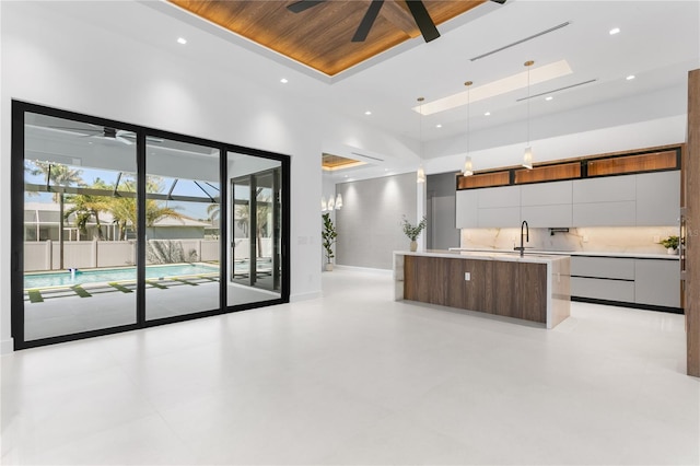 kitchen featuring a sink, a raised ceiling, a ceiling fan, modern cabinets, and a center island