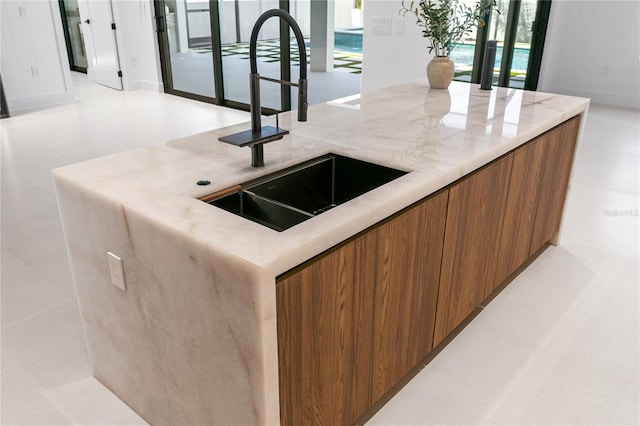 kitchen featuring light stone countertops, a sink, modern cabinets, and brown cabinetry