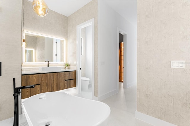 bathroom with baseboards, toilet, a soaking tub, and vanity