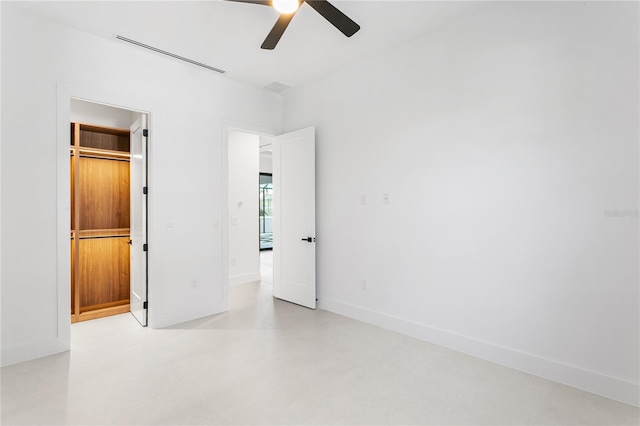 unfurnished bedroom with concrete flooring, a walk in closet, baseboards, visible vents, and ceiling fan