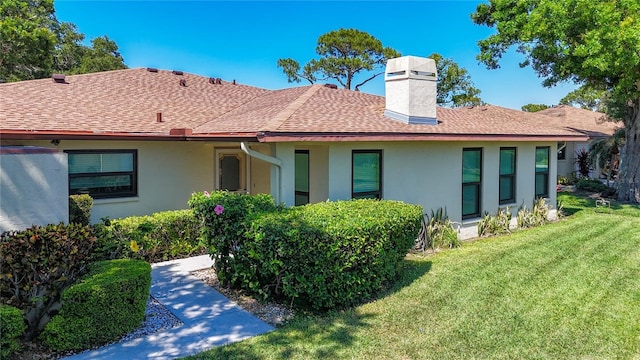 back of property featuring stucco siding, a chimney, a yard, and a shingled roof