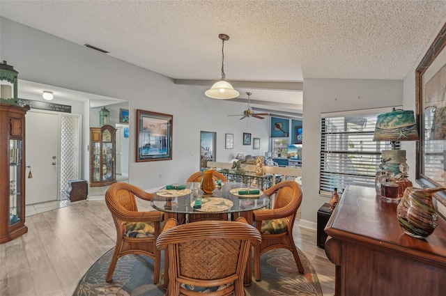 dining area featuring a textured ceiling, visible vents, light wood finished floors, ceiling fan, and lofted ceiling