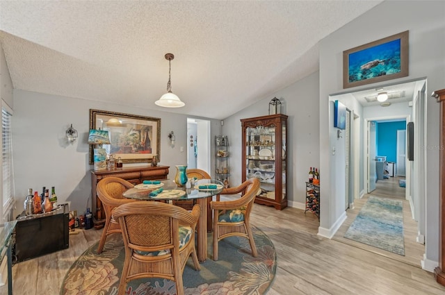 dining space with baseboards, a textured ceiling, vaulted ceiling, and light wood finished floors