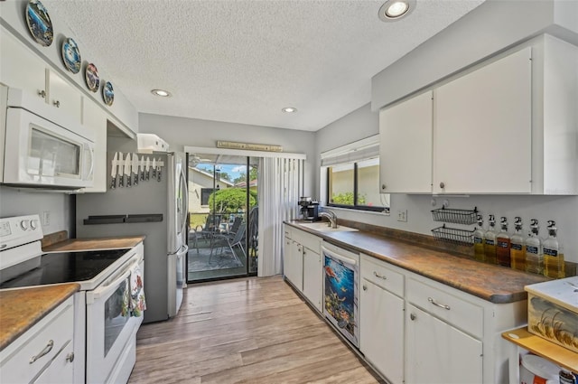 kitchen featuring wine cooler, a sink, white appliances, white cabinets, and light wood-style floors