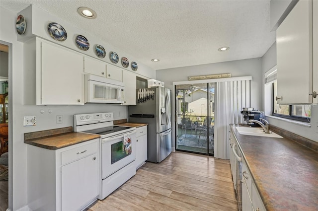 kitchen featuring light wood finished floors, white appliances, dark countertops, white cabinetry, and a sink