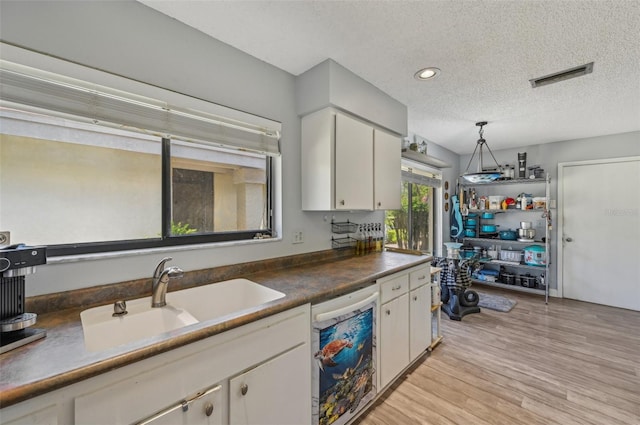 kitchen featuring a sink, dishwashing machine, light wood-style flooring, visible vents, and white cabinets