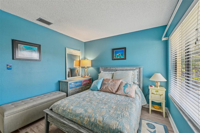 bedroom with wood finished floors, a textured ceiling, baseboards, and visible vents
