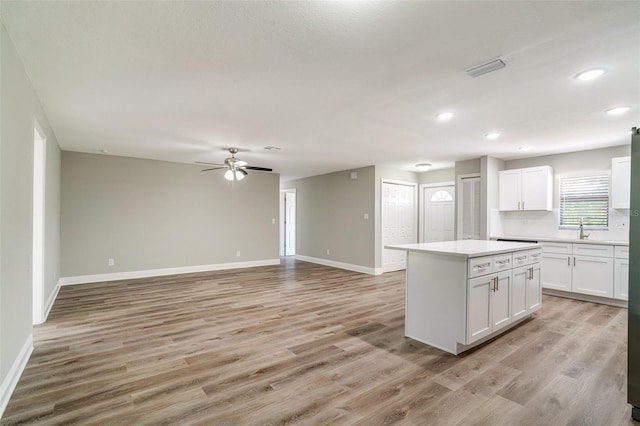 kitchen featuring a kitchen island, a sink, baseboards, white cabinetry, and ceiling fan