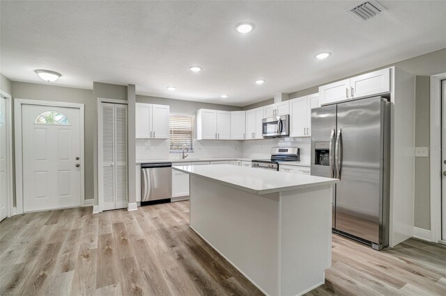 kitchen featuring appliances with stainless steel finishes, light countertops, light wood finished floors, a kitchen island, and white cabinetry