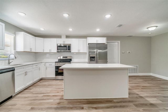 kitchen with stainless steel appliances, a sink, a center island, white cabinets, and recessed lighting