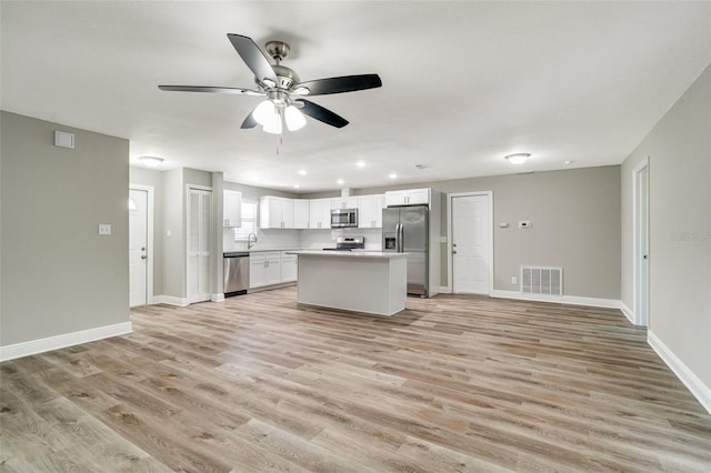 kitchen with appliances with stainless steel finishes, light wood-style flooring, ceiling fan, white cabinetry, and open floor plan