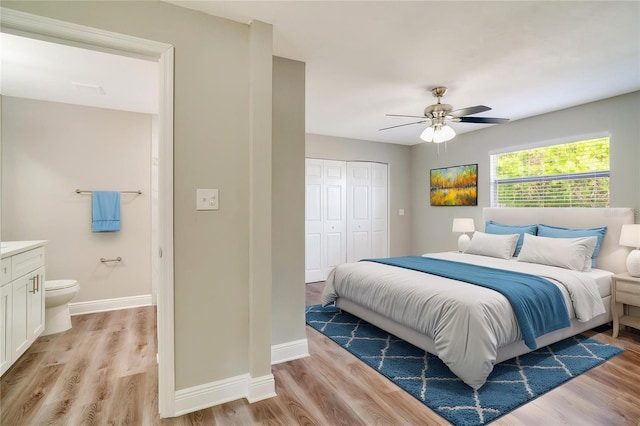 bedroom with a closet, light wood finished floors, baseboards, ensuite bath, and ceiling fan