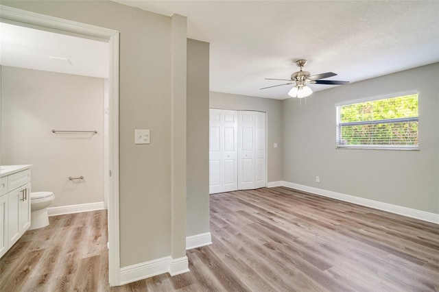 unfurnished bedroom with light wood-style floors, baseboards, a closet, connected bathroom, and ceiling fan