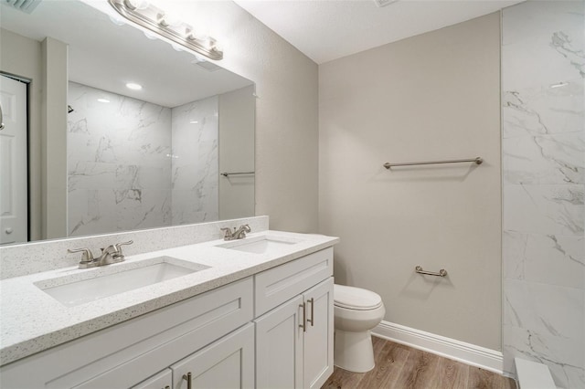 bathroom featuring wood finished floors, toilet, double vanity, baseboards, and a marble finish shower