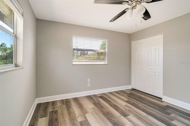 unfurnished bedroom featuring wood finished floors, a closet, baseboards, and a ceiling fan