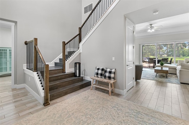 staircase with wood finish floors, visible vents, ceiling fan, and baseboards