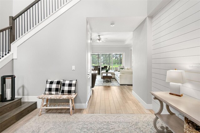 entryway with light wood finished floors, stairway, ceiling fan, wood walls, and baseboards