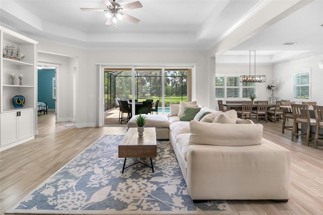 living area featuring light wood-type flooring, plenty of natural light, a tray ceiling, and ceiling fan with notable chandelier
