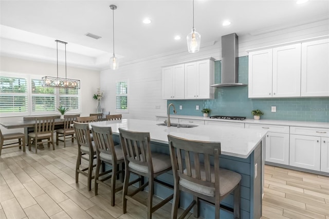kitchen featuring decorative backsplash, light countertops, a sink, visible vents, and wall chimney exhaust hood