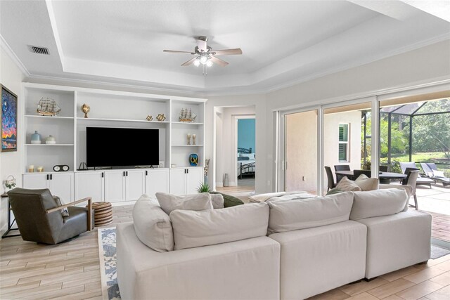 living area featuring a raised ceiling, visible vents, a ceiling fan, and light wood-style flooring