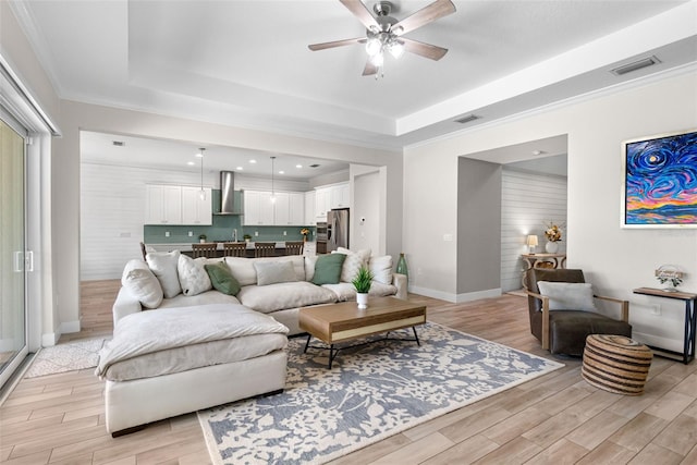 living area with visible vents, ceiling fan, light wood-style flooring, and a tray ceiling