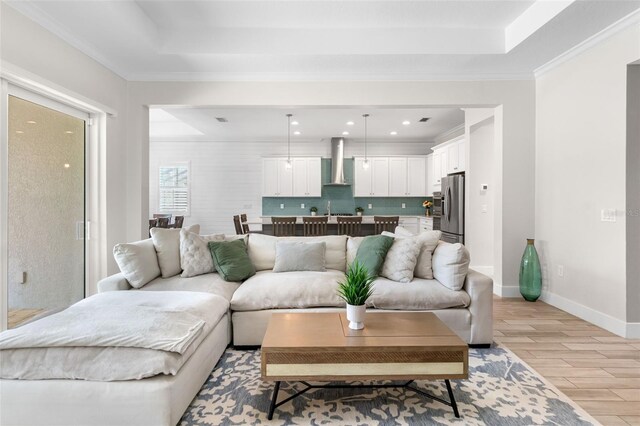 living room featuring baseboards, recessed lighting, a raised ceiling, and light wood-style floors