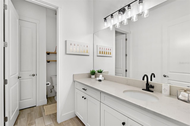 bathroom with baseboards, wood finished floors, toilet, and vanity