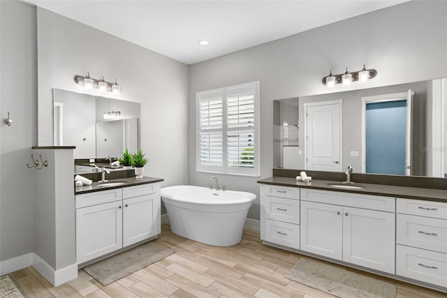 full bath with wood finished floors, a freestanding bath, and a sink